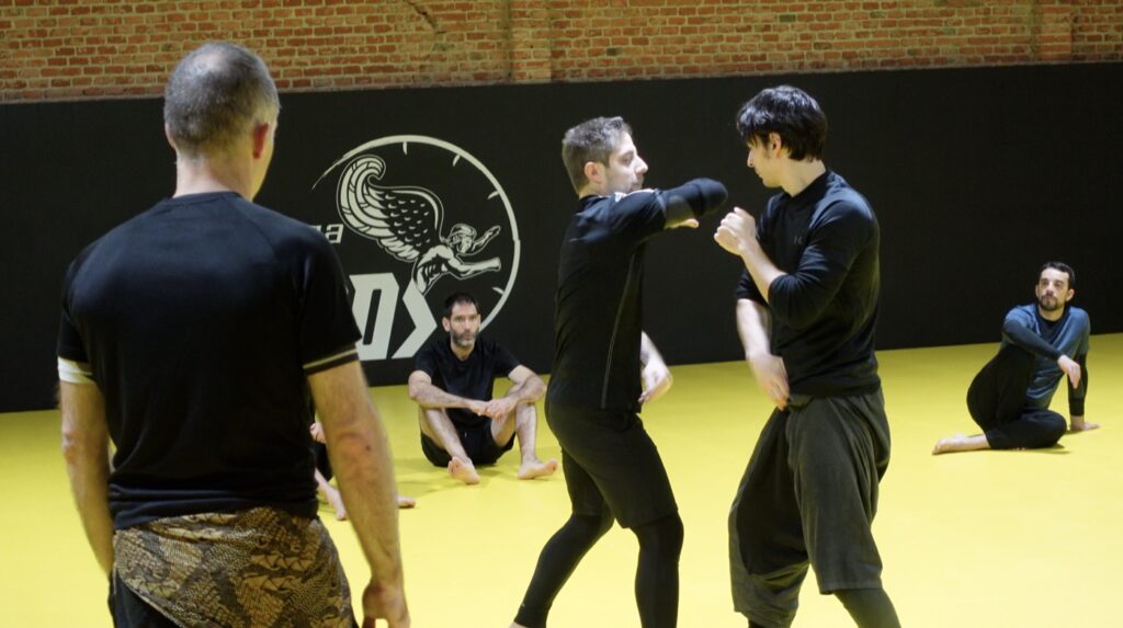Dos alumnos practicando de pie mientras Sebastián Deibe observa